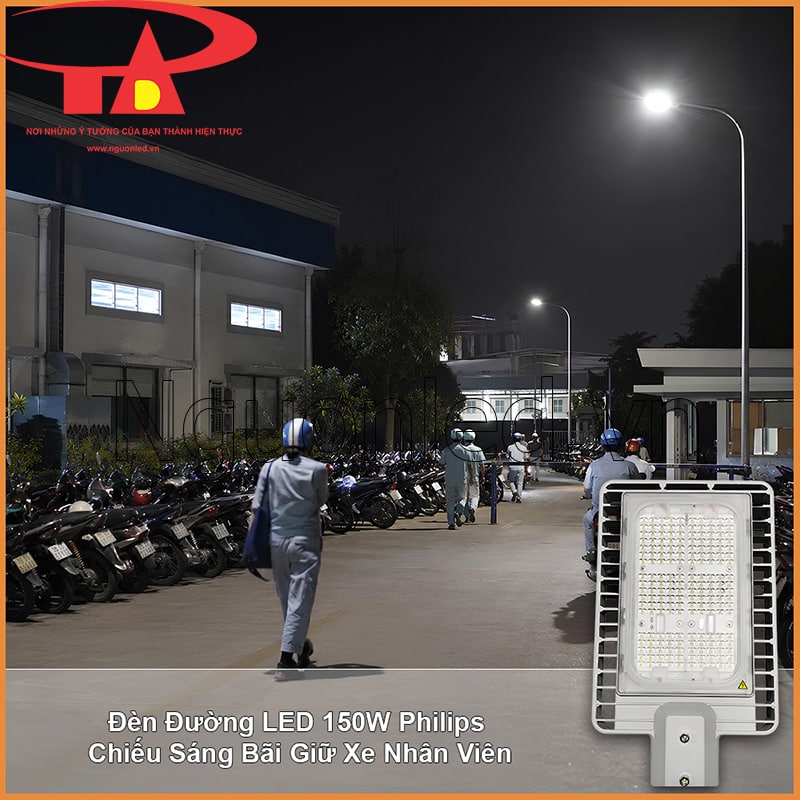 Bãi giữ xe nhân viên với nhiều xe máy, người đi bộ và lối di chuyển được chiếu sáng vào ban đêm