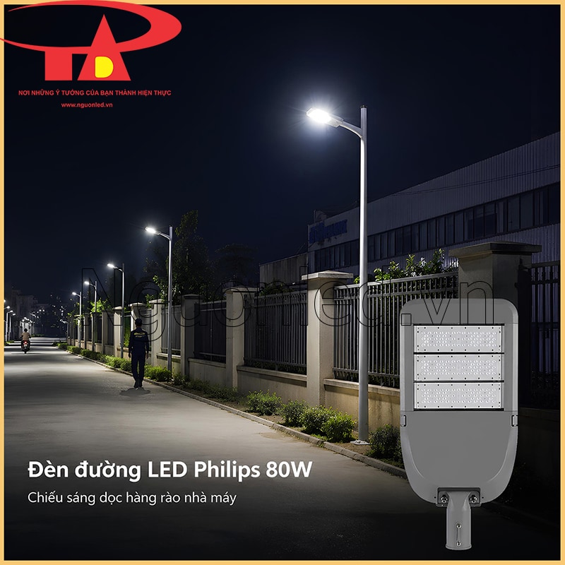 Đèn đường 80W chiếu dọc đoạn hàng rào nhà máy vào ban đêm, có lối đi bộ và các cột đèn nối tiếp