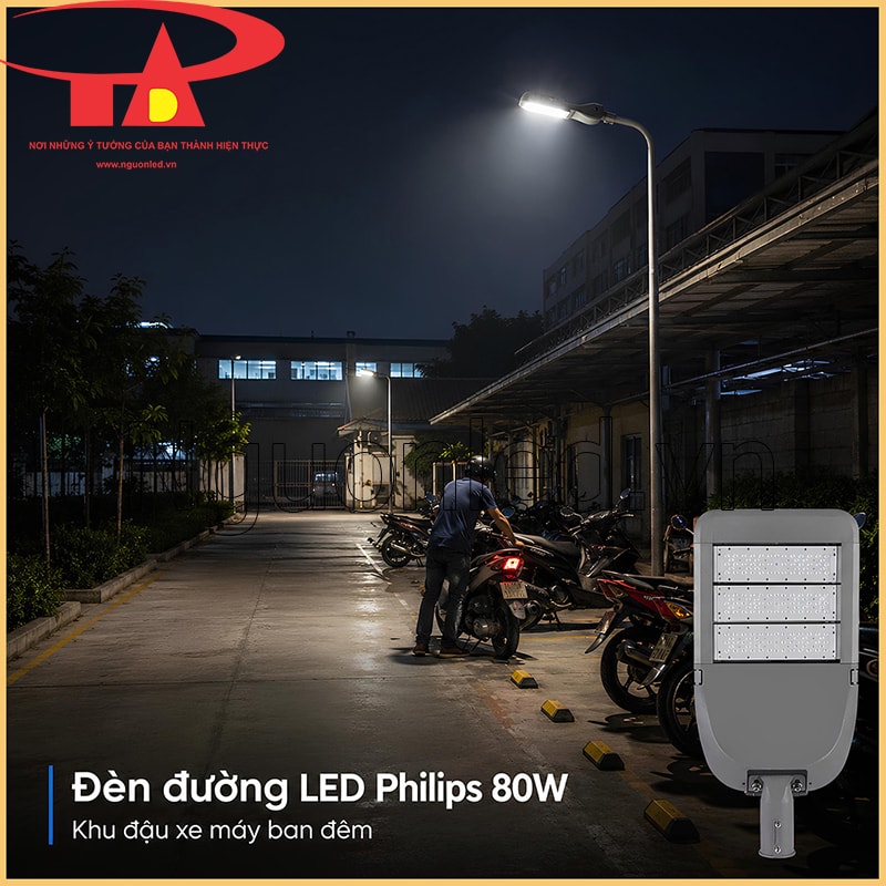  Đèn đường Philips 80W chiếu bãi đậu xe máy ban đêm, có người dắt xe và phần mép sân phía trước
